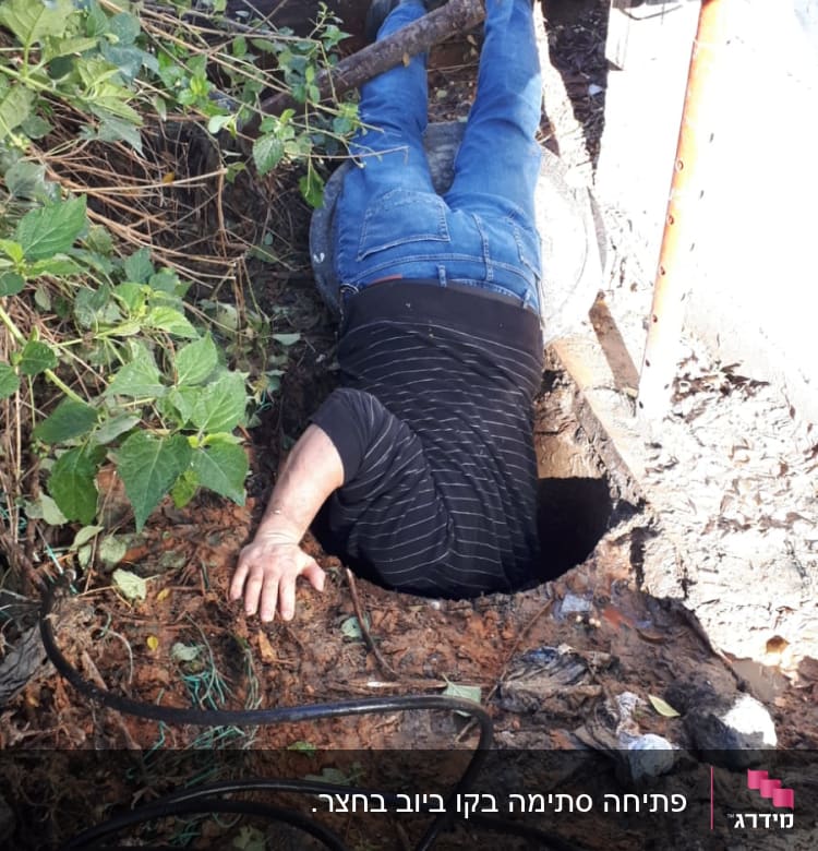 אדם שוכב על הקרקע ליד חור עם צינורות